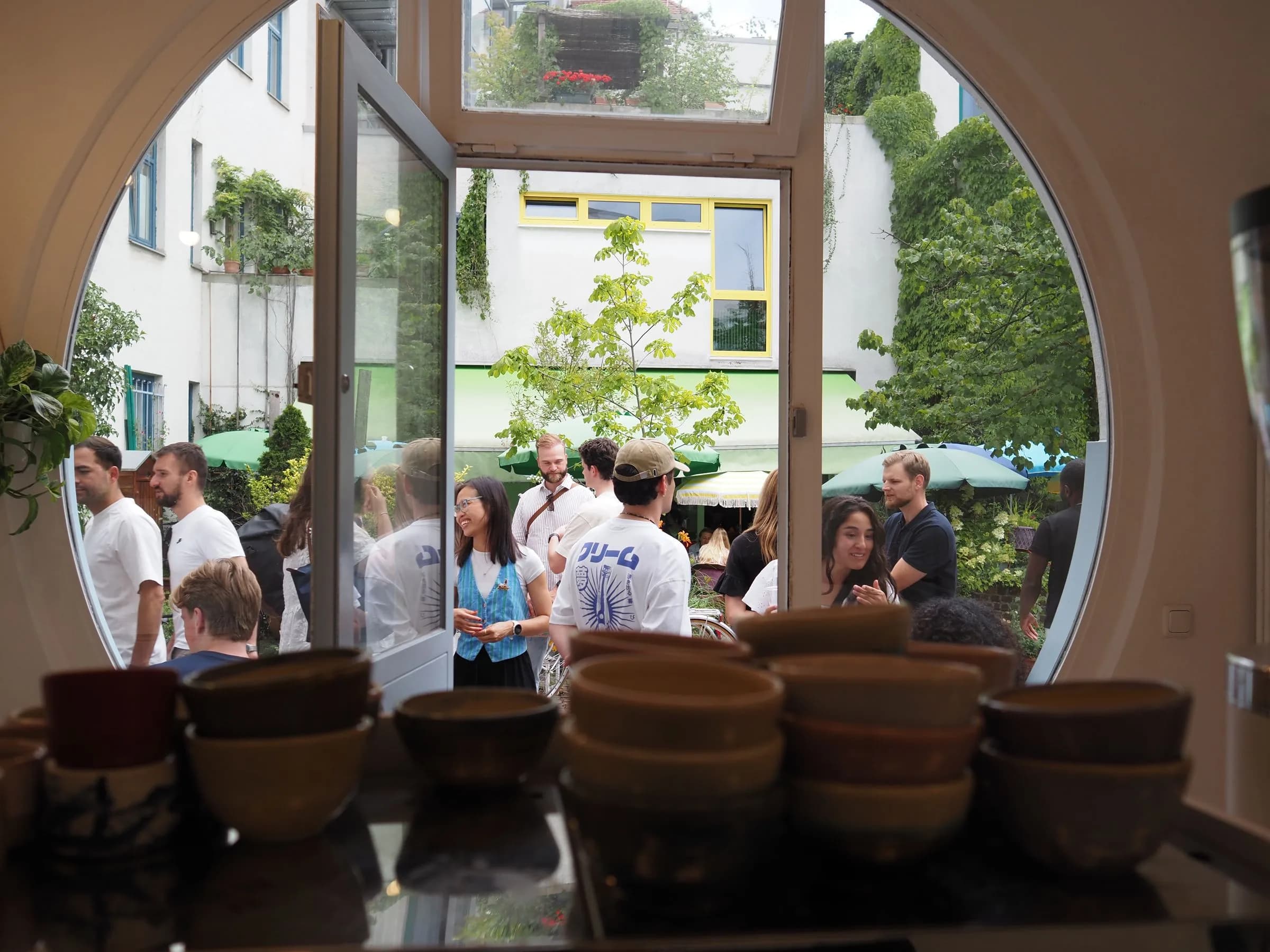 Handmade ceramic cups by the café's porthole doorway, looking out to a busy Amalienpassage courtyard in Munich