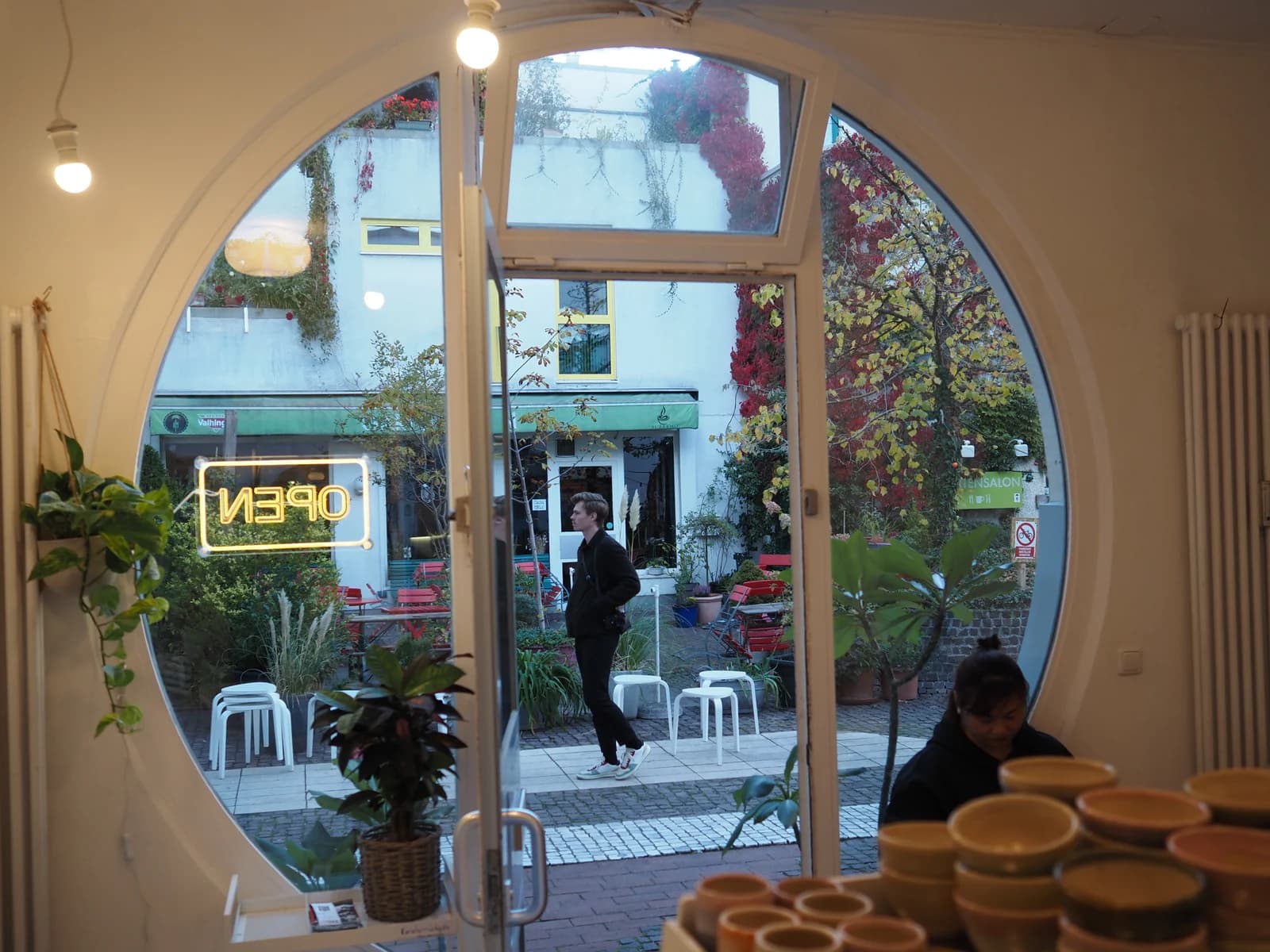 Der Hof der Amalienpassage im Herbst, von innen durch die runde Bullaugentür von Humpback Whale Coffee gesehen, München