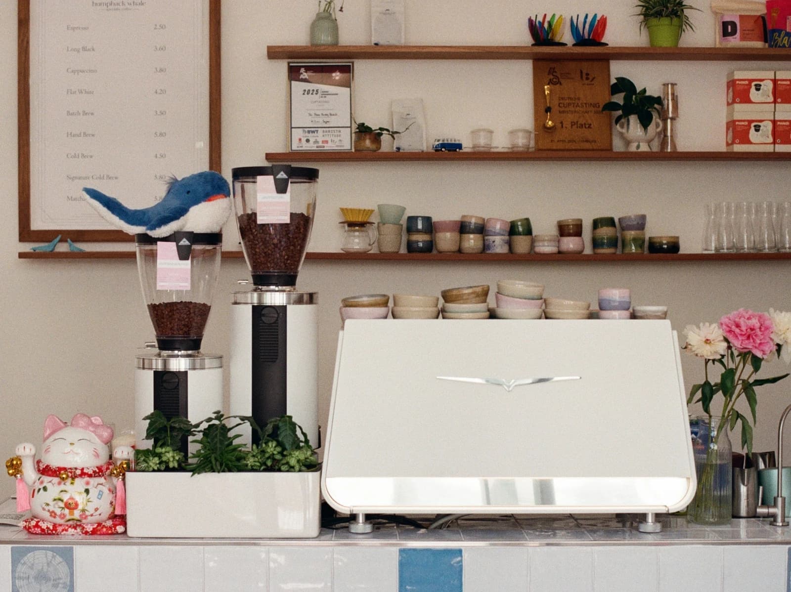 Die Café-Bar von Humpback Whale in München — Espressomaschine, handgefertigte Keramiktassen und der Pokal der Deutschen Cuptasting-Meisterschaft 2025 im Regal