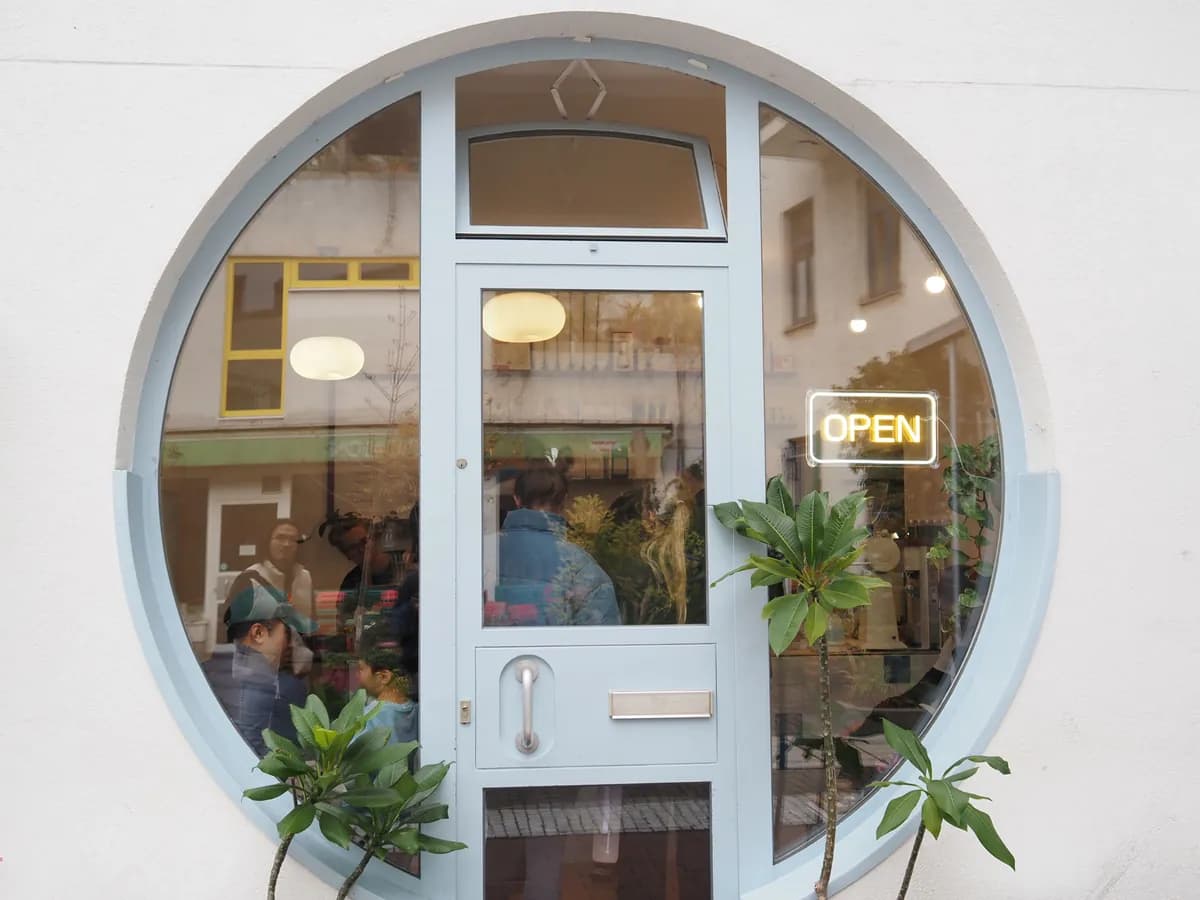 The Humpback Whale café's round porthole window in Munich, lit 'Open', with guests inside